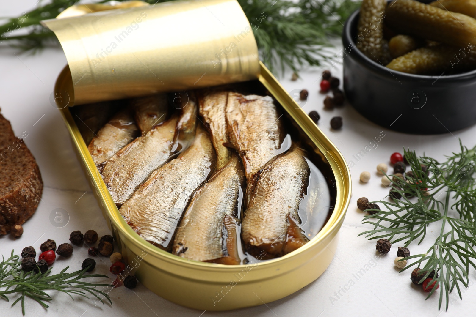 Photo of Tasty sprats in tin can served on white table, closeup