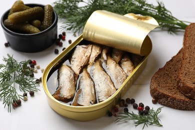 Photo of Tasty sprats in tin can served on white table, closeup