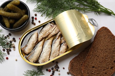 Tasty sprats in tin can served on white tiled table, flat lay