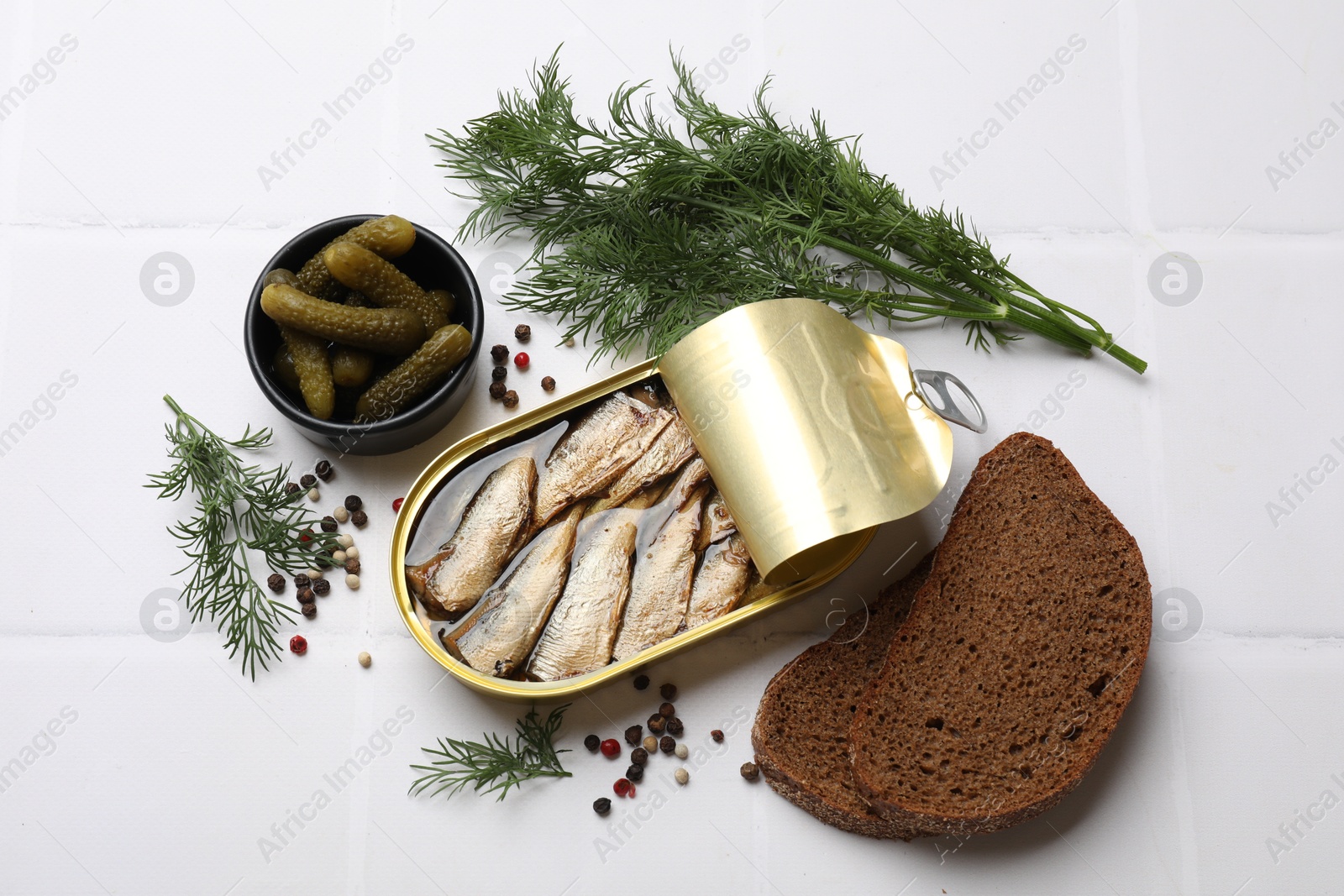 Photo of Tasty sprats in tin can served on white tiled table, flat lay