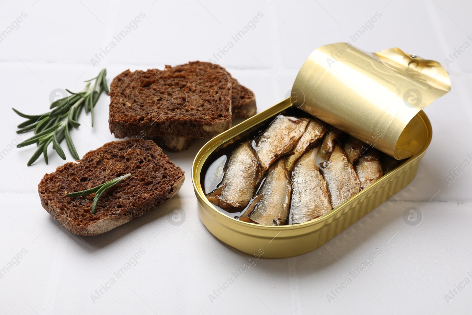 Photo of Tasty sprats in tin can served on white tiled table