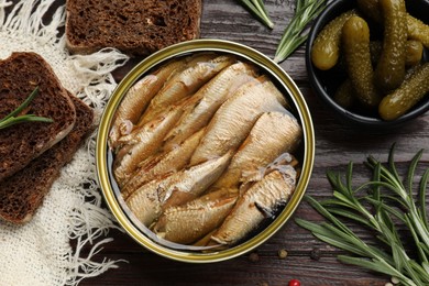 Tasty sprats in tin can served on wooden table, flat lay