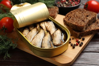 Photo of Tasty sprats in tin can served on wooden table, closeup