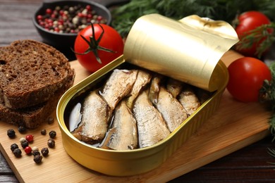 Tasty sprats in tin can served on wooden table, closeup