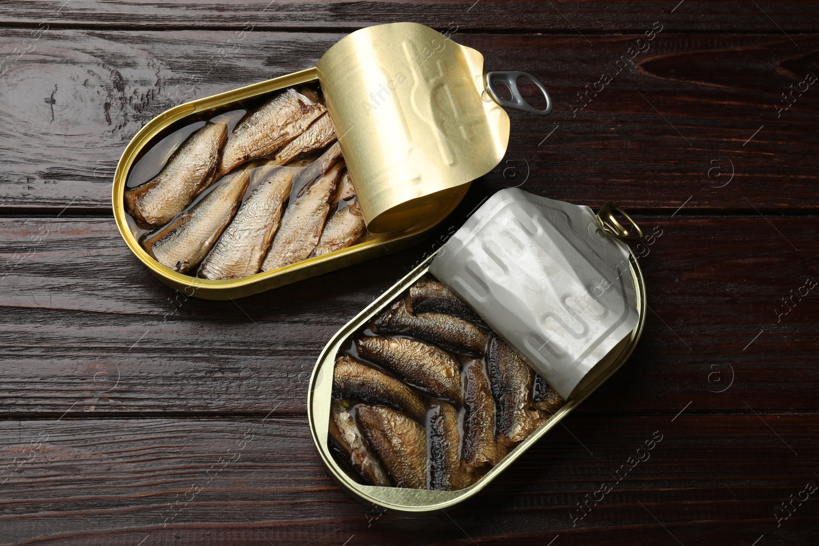 Photo of Tasty sprats in tin cans on wooden table, flat lay