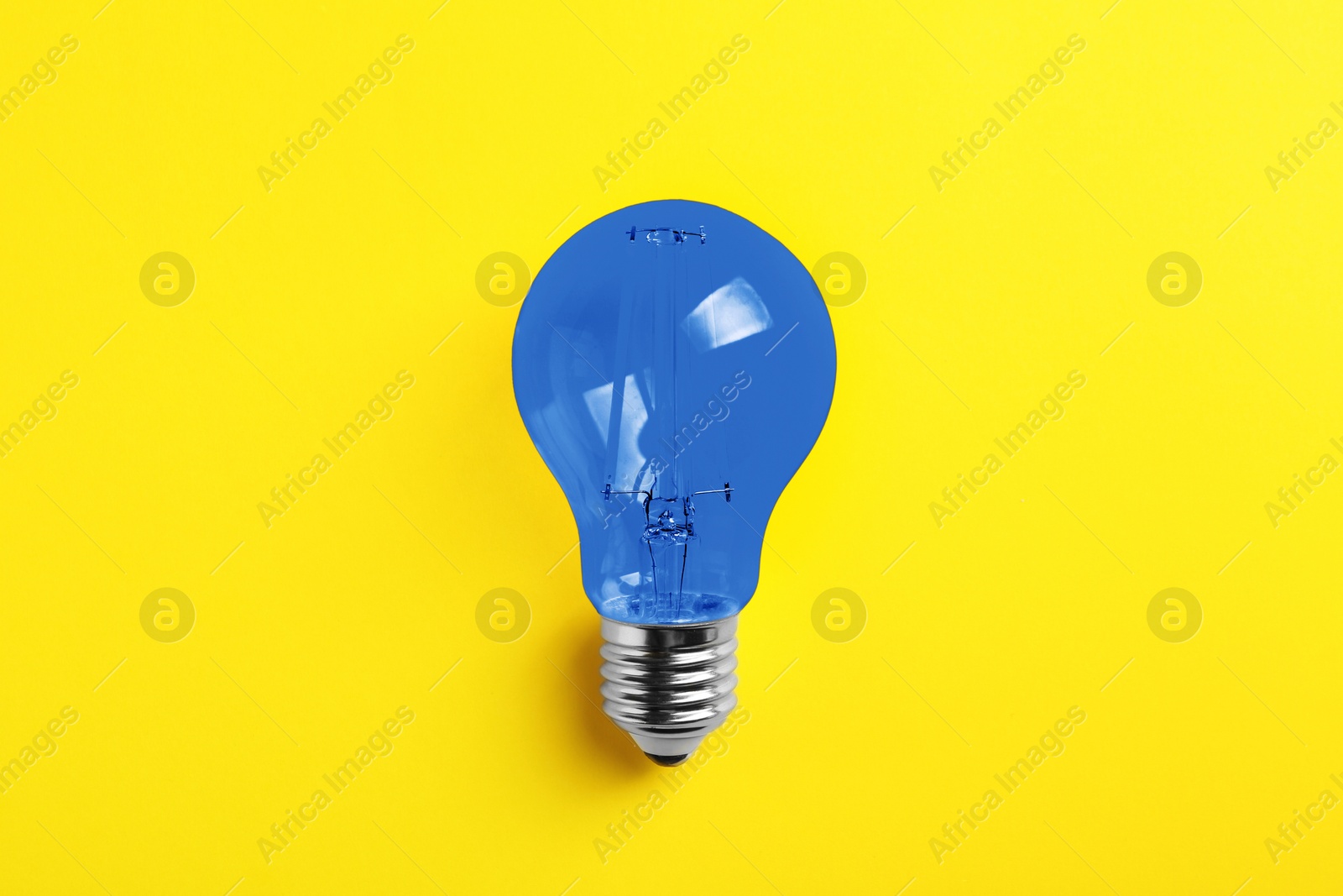 Image of One blue light bulb on yellow background