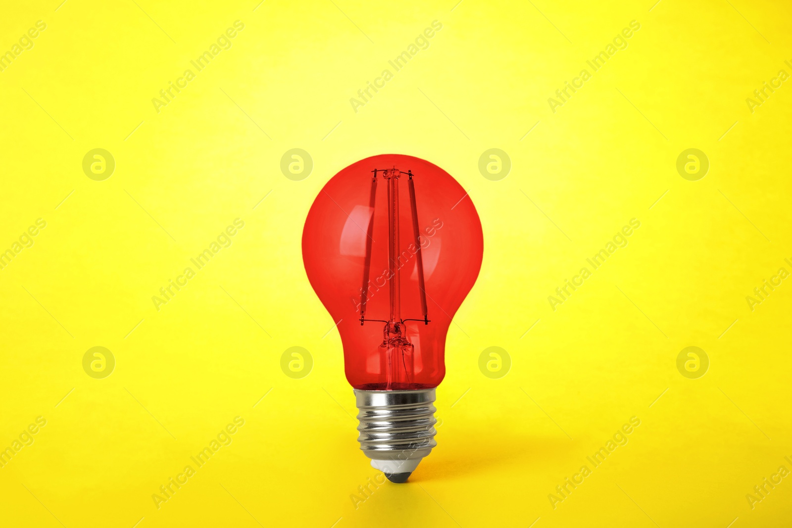 Image of One red light bulb on yellow background