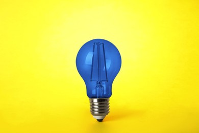 Image of One blue light bulb on yellow background