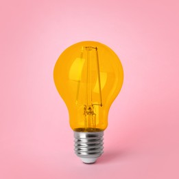 Image of One orange light bulb on pink background