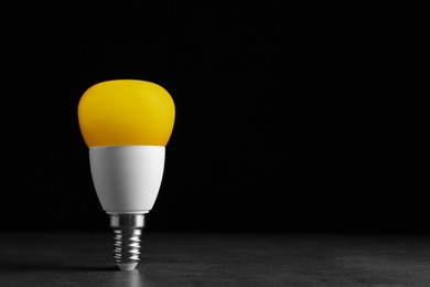 Image of Yellow light bulb against black background, space for text