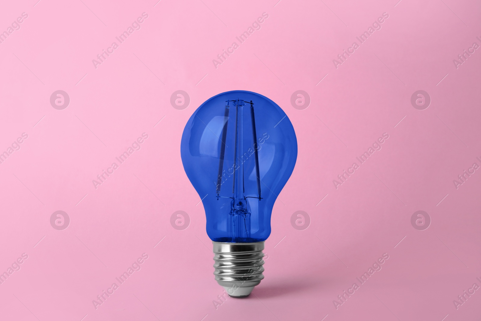 Image of One blue light bulb on pink background