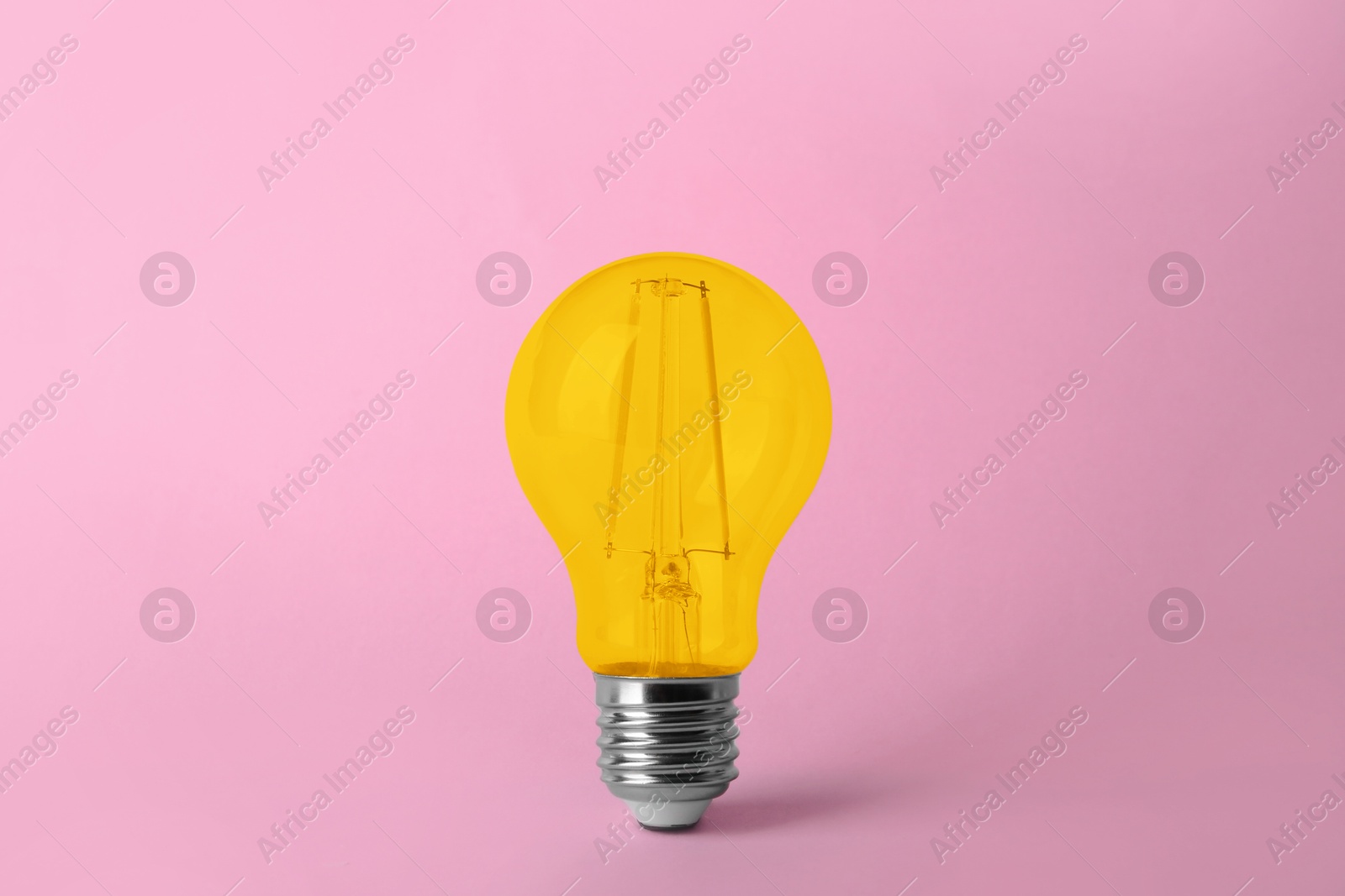 Image of One yellow light bulb on pink background