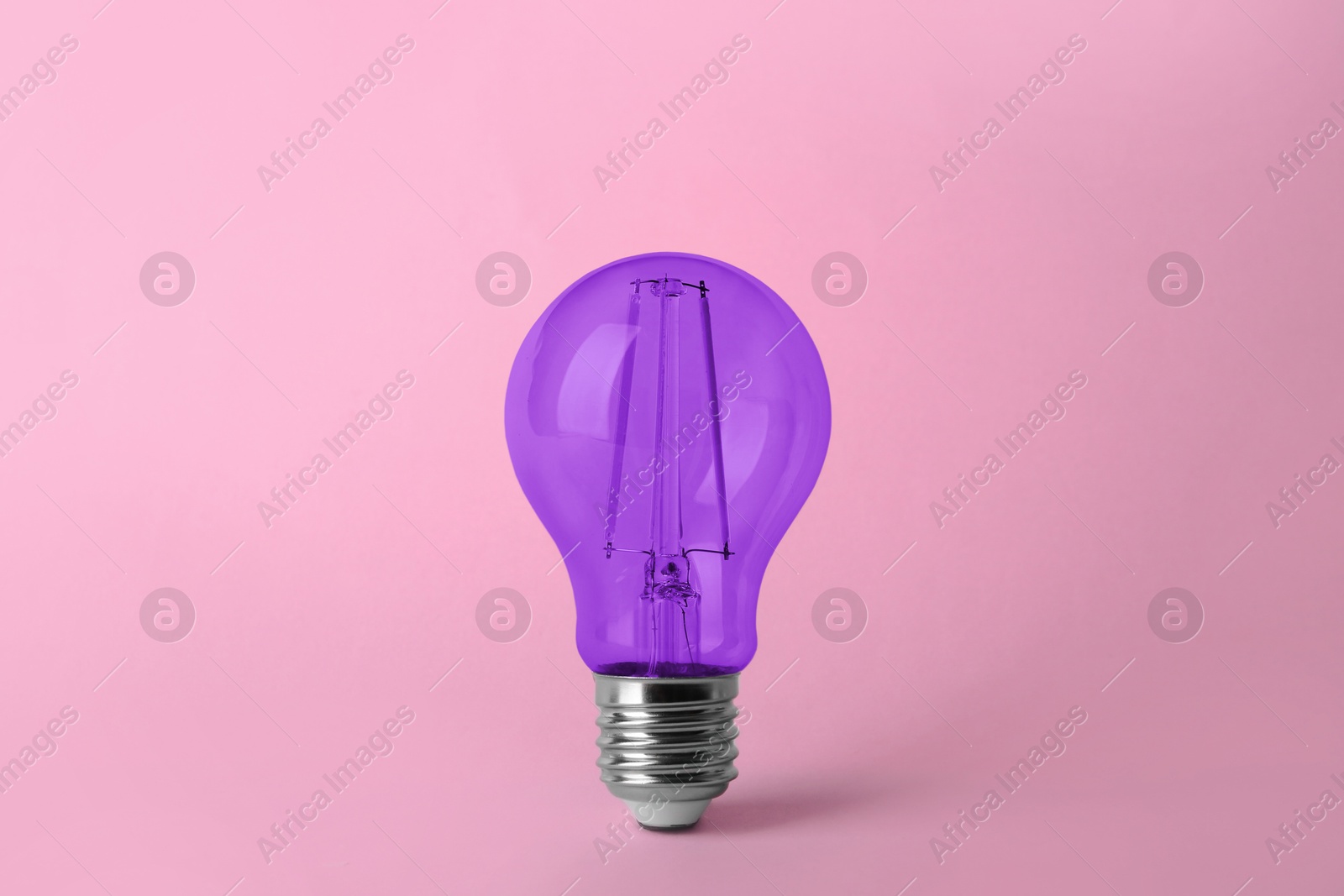 Image of One violet light bulb on pink background