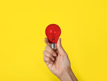 Image of Woman holding red light bulb on yellow background, closeup