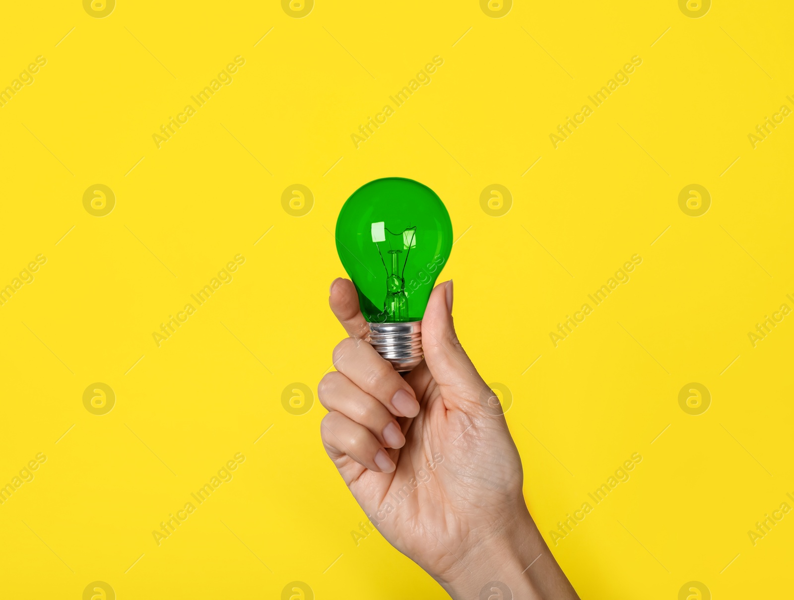 Image of Woman holding green light bulb on yellow background, closeup