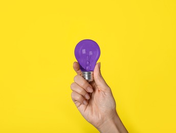 Woman holding violet light bulb on yellow background, closeup