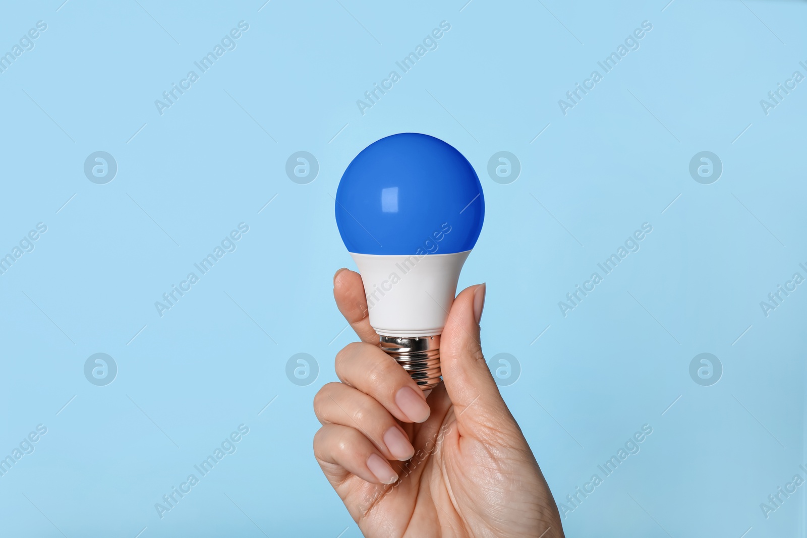 Image of Woman holding blue bulb on light blue background, closeup