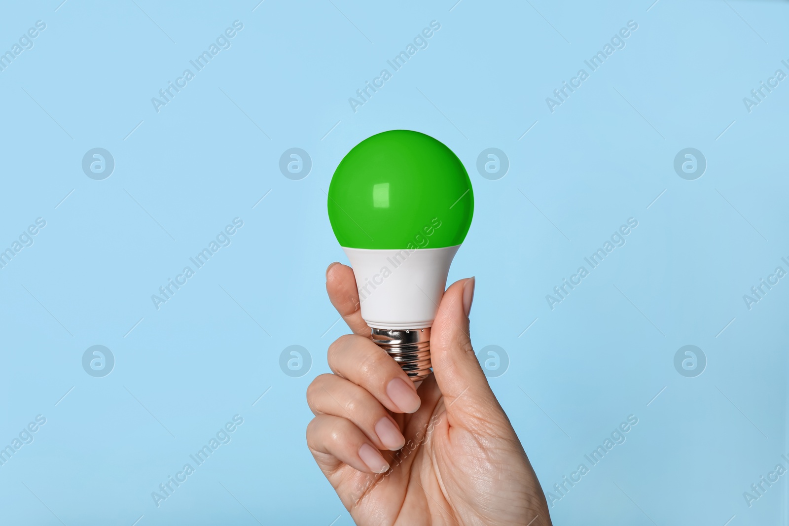 Image of Woman holding green bulb on light blue background, closeup