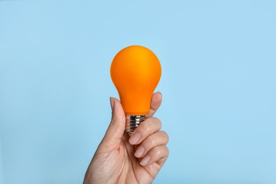 Image of Woman holding orange bulb on light blue background, closeup