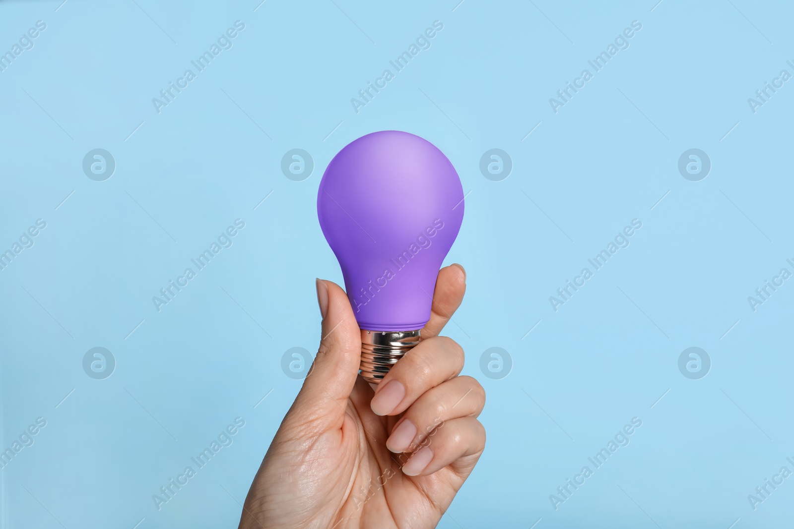 Image of Woman holding violet bulb on light blue background, closeup