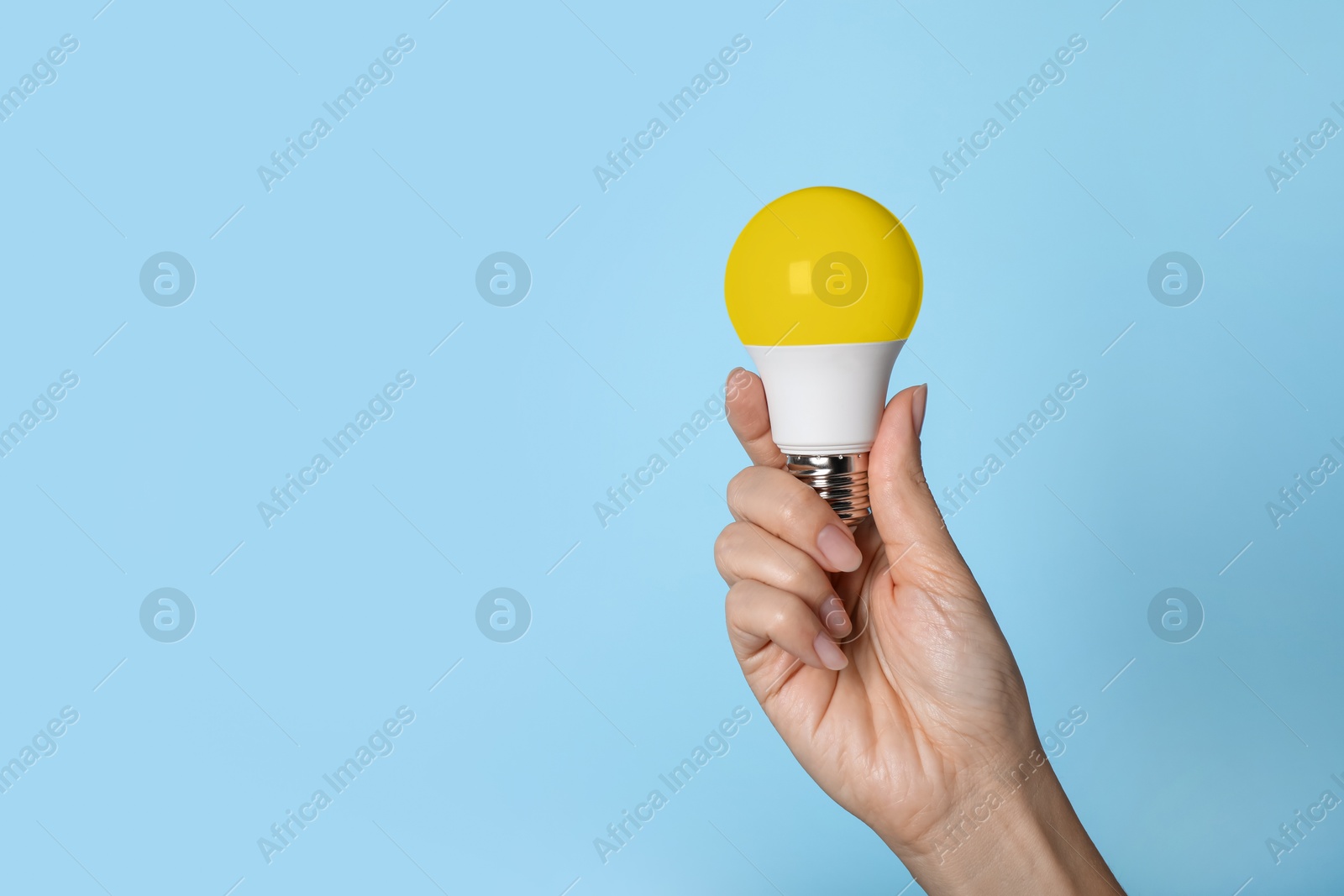 Image of Woman holding yellow bulb on light blue background, closeup. Space for text