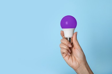 Image of Woman holding purple bulb on light blue background, closeup. Space for text