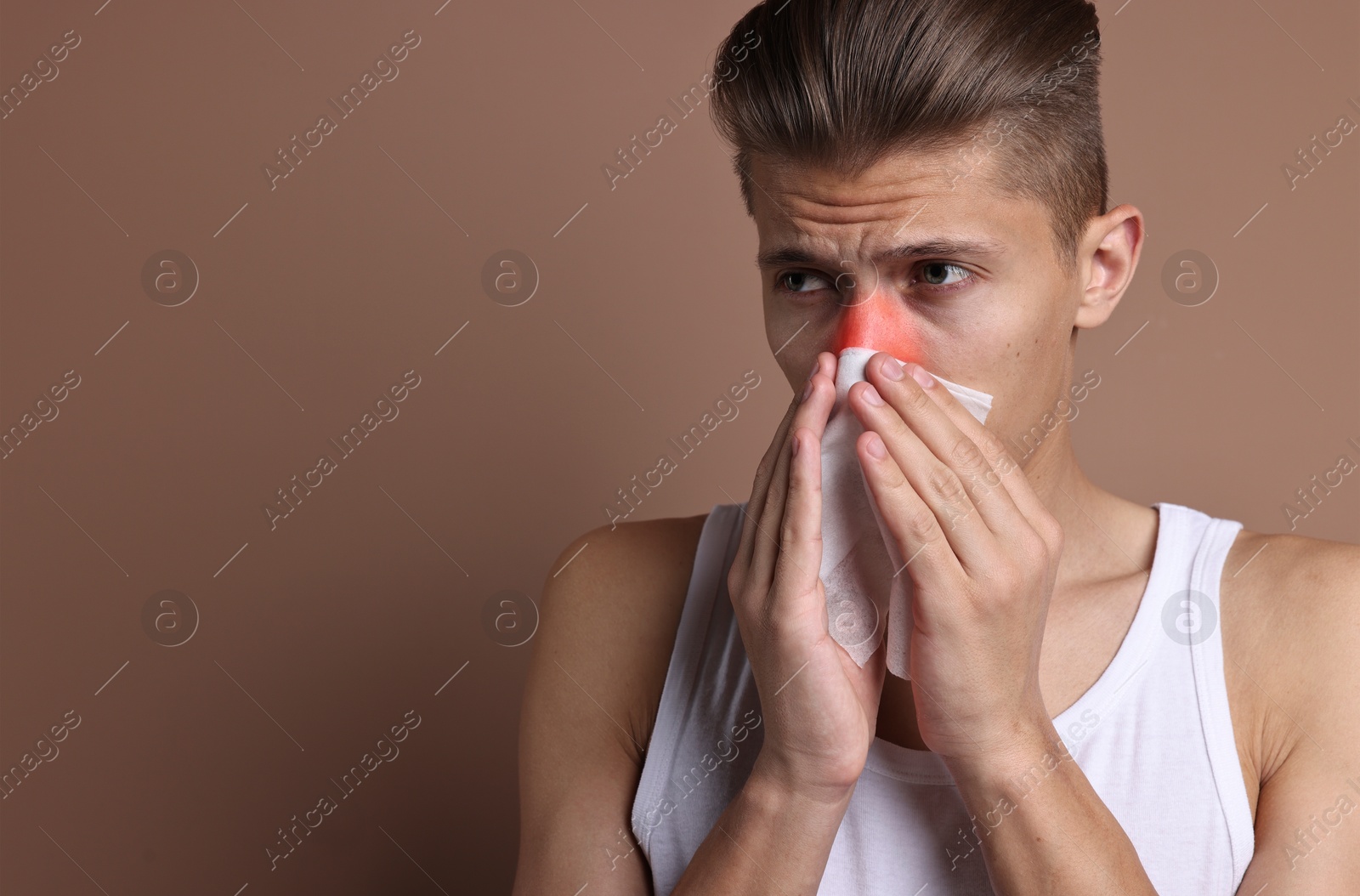 Image of Young man with tissue suffering from sinusitis on light brown background, space for text