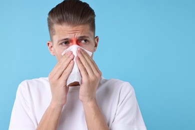 Young man with tissue suffering from sinusitis on light blue background, space for text