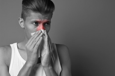 Young man with tissue suffering from sinusitis, space for text. Black and white effect with red color accent