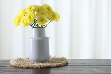 Photo of Beautiful yellow flowers in vase on wooden table at home. Space for text