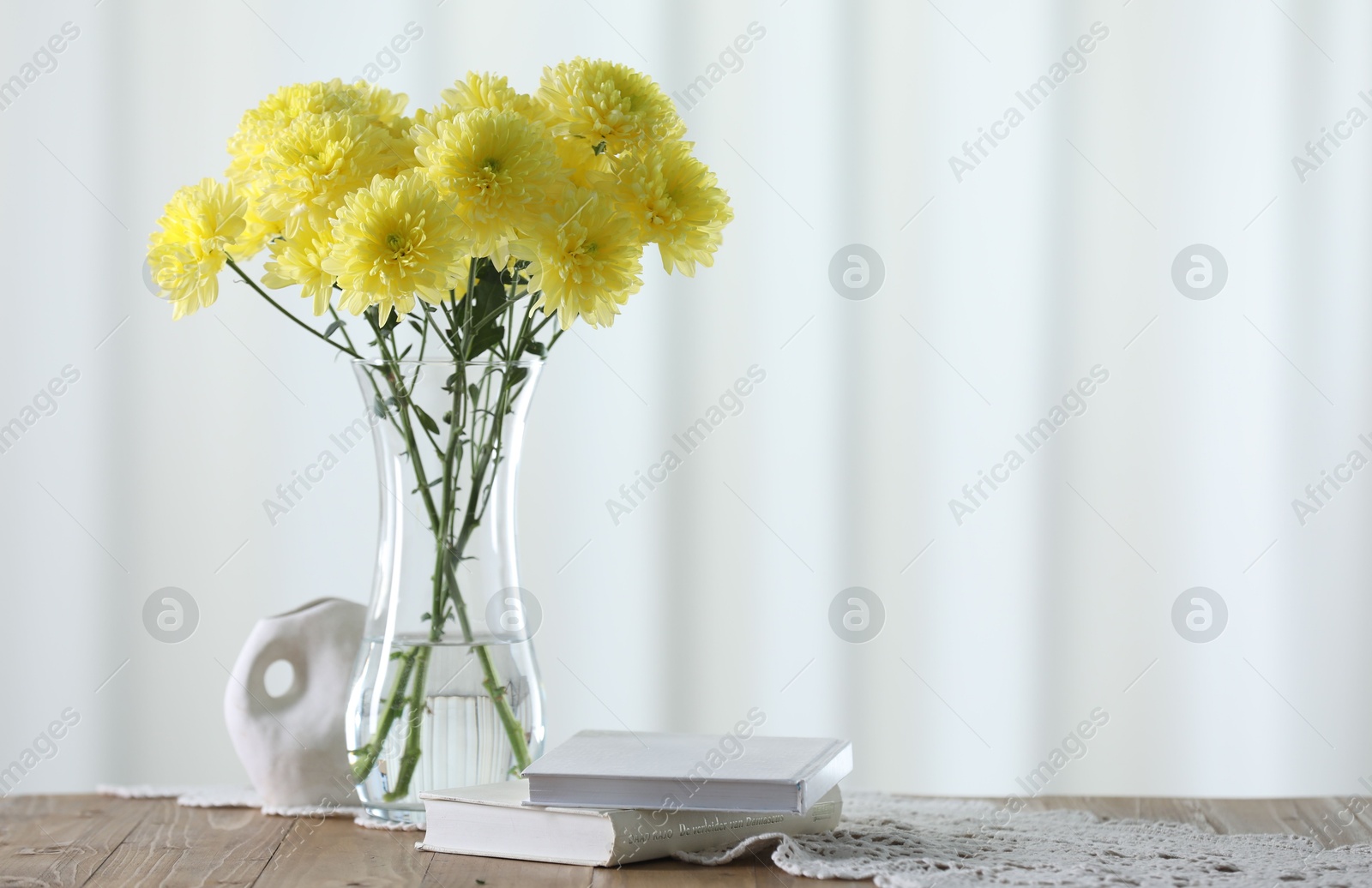 Photo of Beautiful yellow flowers in vase and books on wooden table at home. Space for text