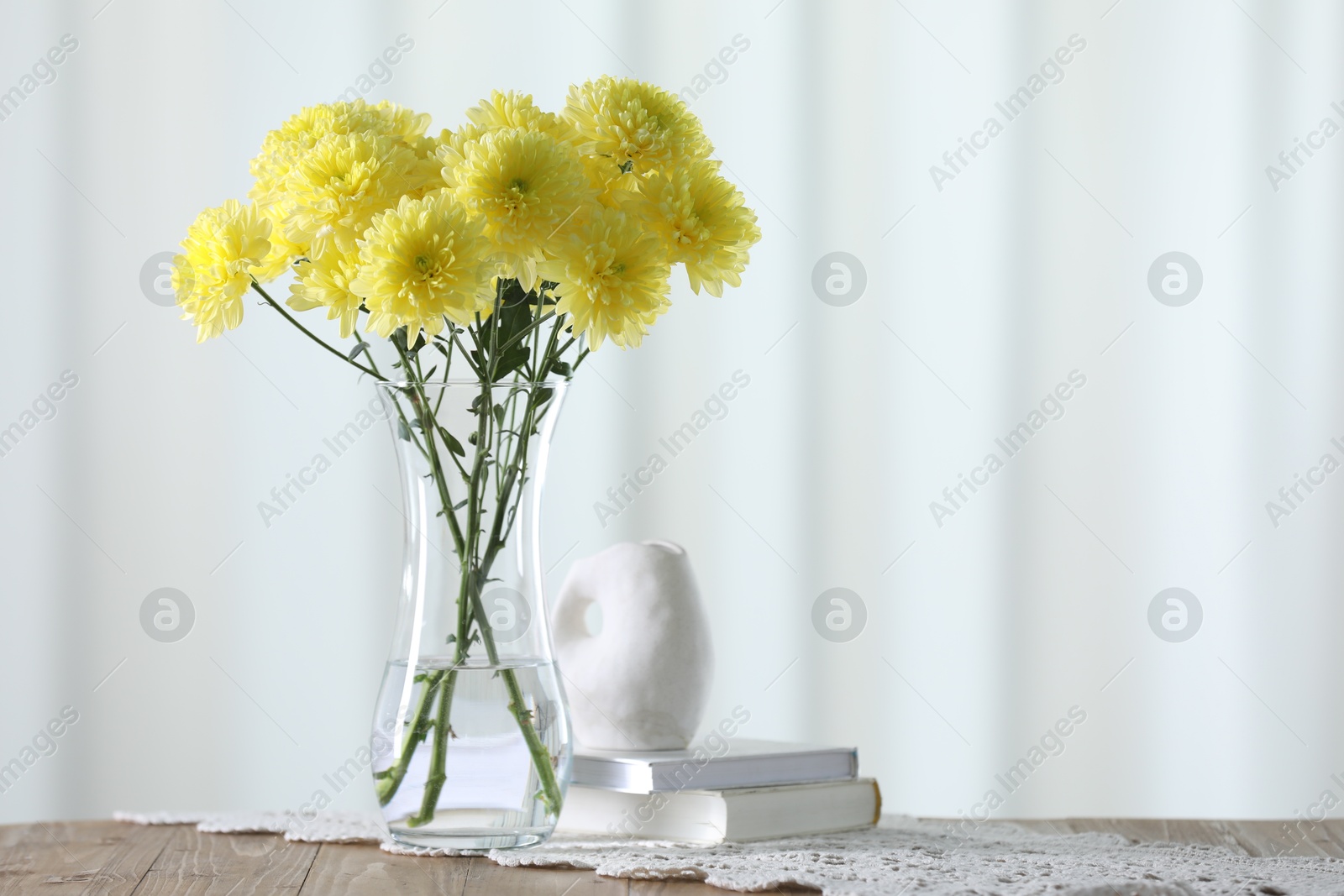 Beautiful yellow flowers in vase and books on wooden table at home. Space for text Photo of Beautiful yellow flowers in vase and books on wooden table at home. Space for text
