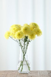 Photo of Beautiful yellow flowers in vase on wooden table at home