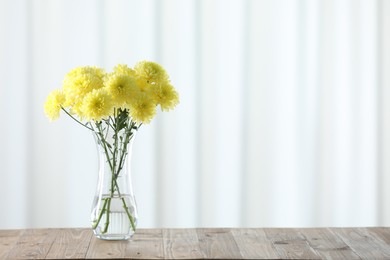 Photo of Beautiful yellow flowers in vase on wooden table at home. Space for text