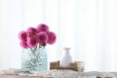 Photo of Beautiful pink flowers in vase on wooden table at home. Space for text