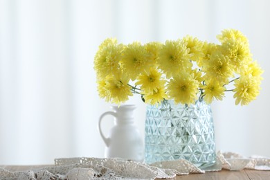 Photo of Beautiful yellow flowers in vase on wooden table at home. Space for text