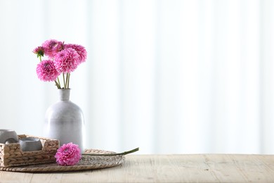 Photo of Beautiful pink flowers in vase and burning candle on wooden table at home. Space for text