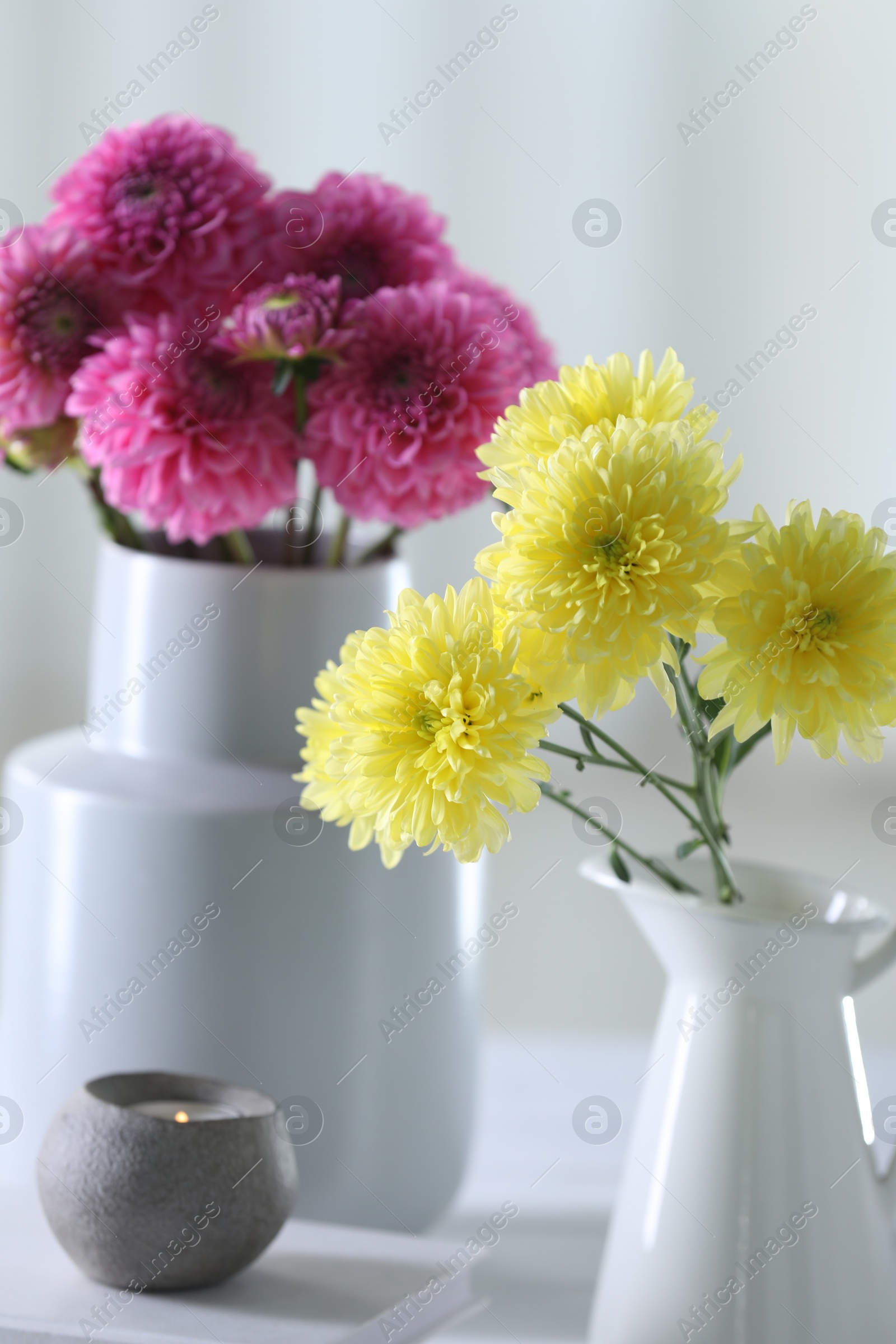 Photo of Beautiful flowers in vases and burning candle on light table at home, closeup