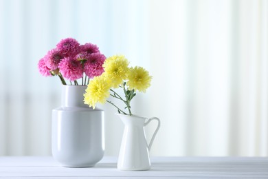 Photo of Beautiful yellow and pink flowers in vases on white wooden table at home. Space for text