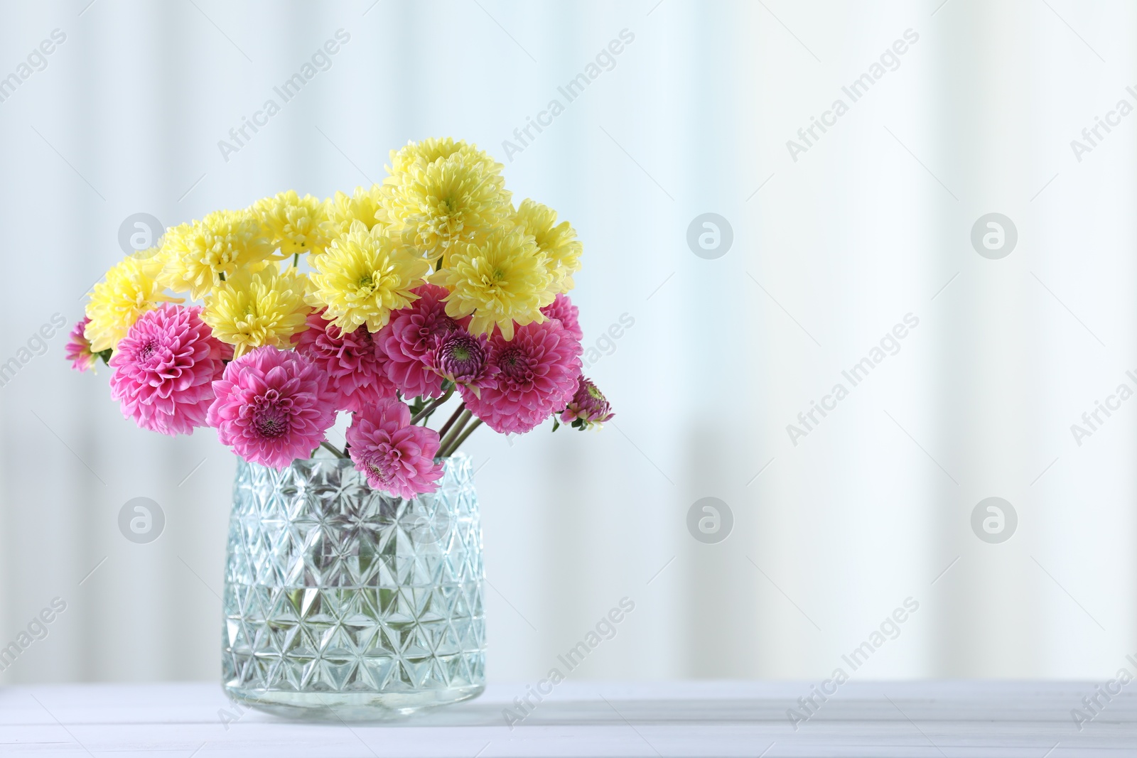 Beautiful yellow and pink flowers in vase on white wooden table at home. Space for text Photo of Beautiful yellow and pink flowers in vase on white wooden table at home. Space for text