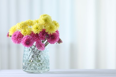 Photo of Beautiful yellow and pink flowers in vase on white wooden table at home. Space for text