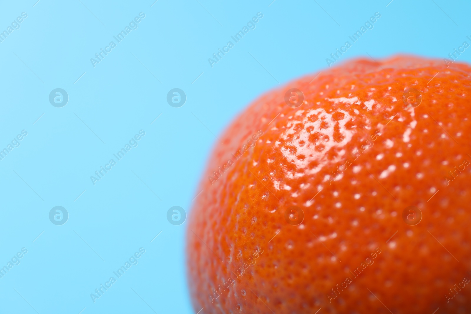 Photo of Fresh ripe tangerine on light blue background, closeup. Space for text