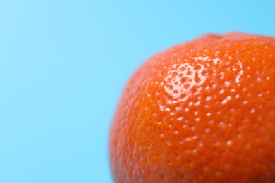 Photo of Fresh ripe tangerine on light blue background, closeup. Space for text