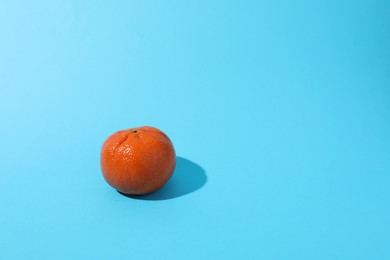 Photo of Fresh ripe tangerine on light blue background. Space for text