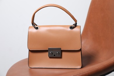 Stylish dark beige leather bag on brown chair, closeup