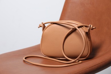 Stylish dark beige leather bag on brown chair, closeup