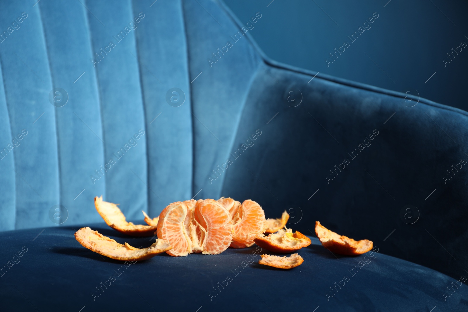 Photo of Fresh peeled tangerine on dark blue armchair