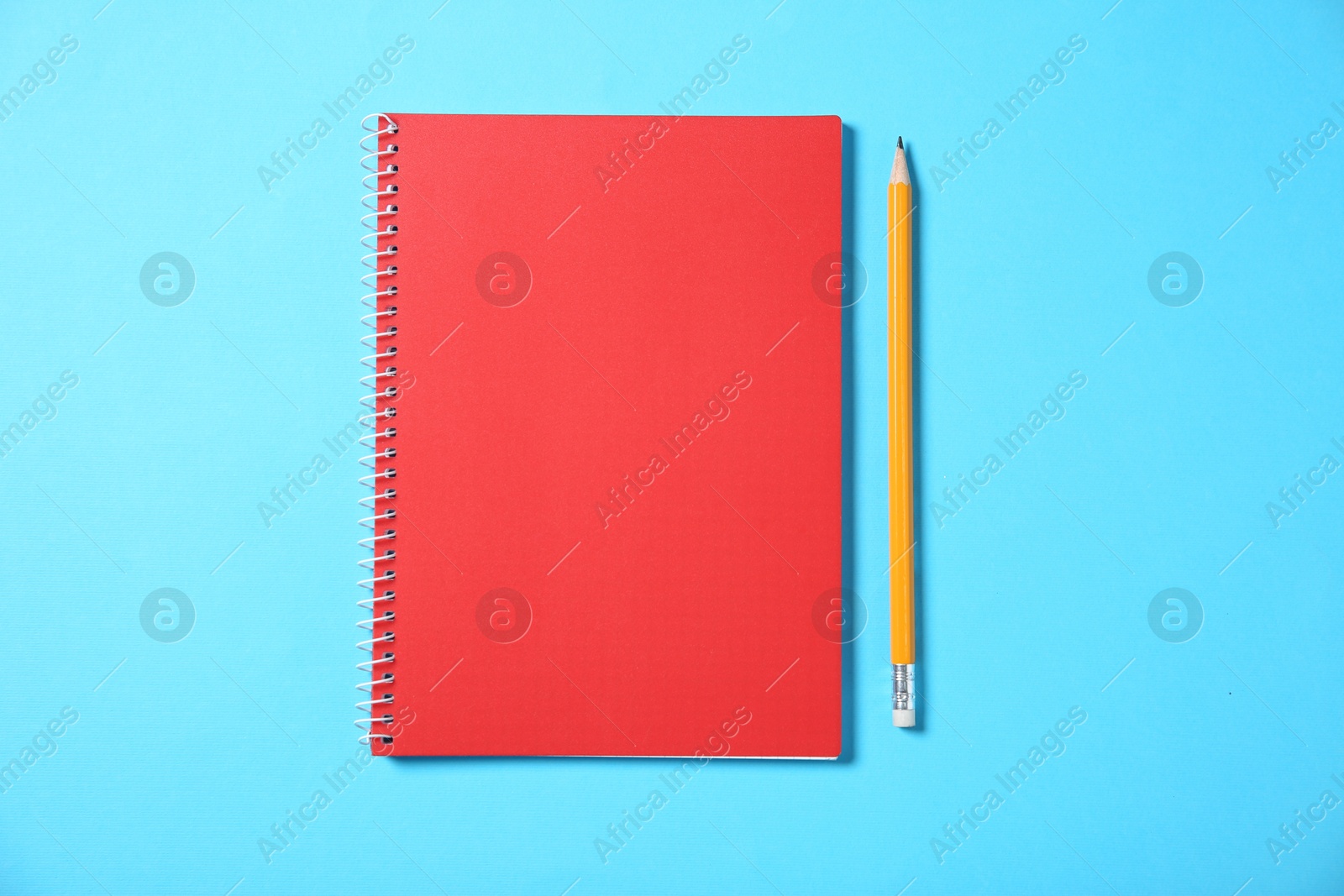 Photo of Notebook and pencil on light blue background, top view