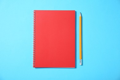 Notebook and pencil on light blue background, top view