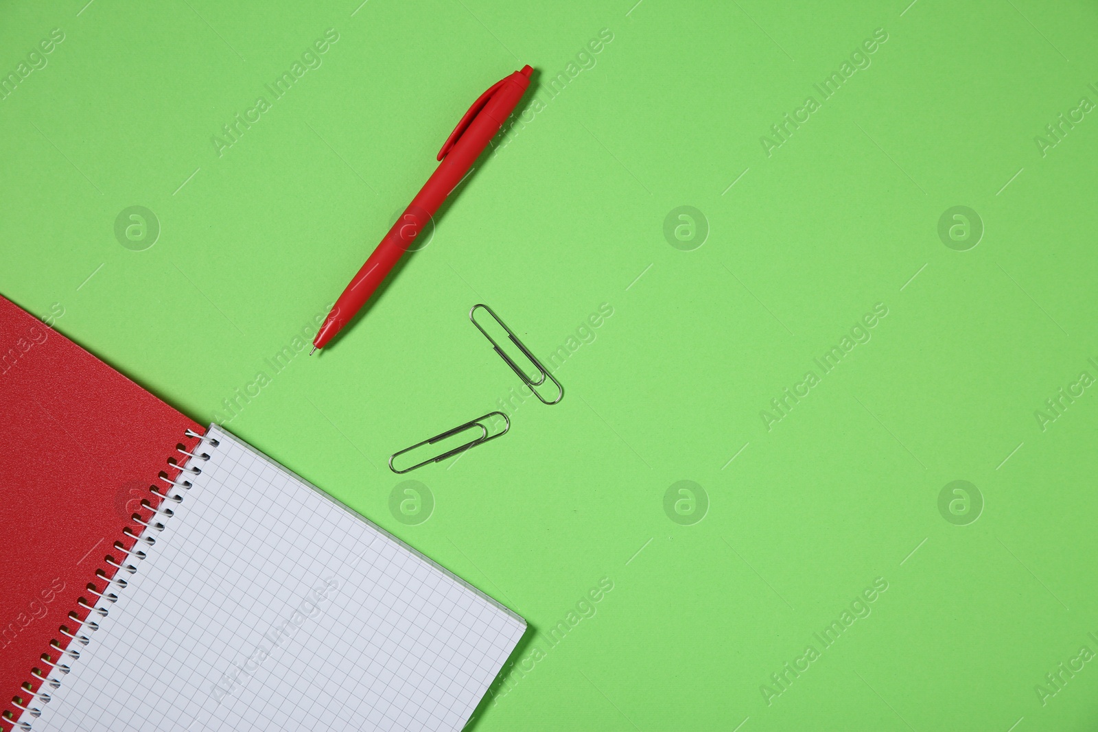 Photo of Notebook, paper clips and pen on light green background, top view. Space for text